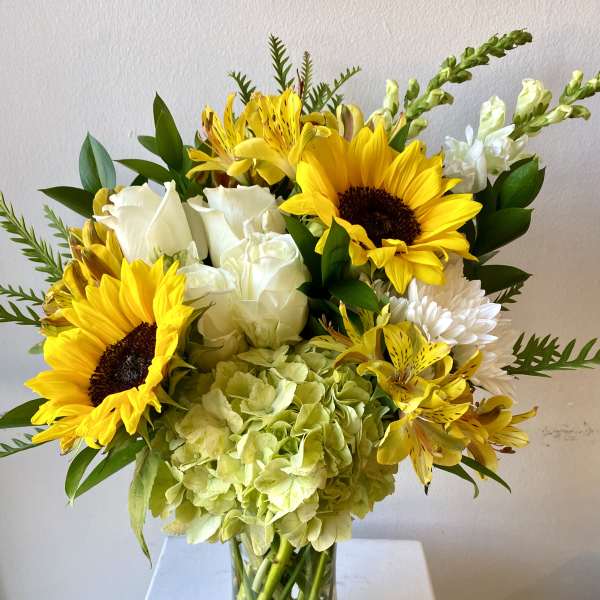 Glass vase of yellow sunflowers, white roses, green hydrangea, and mixed yellow and white flowers