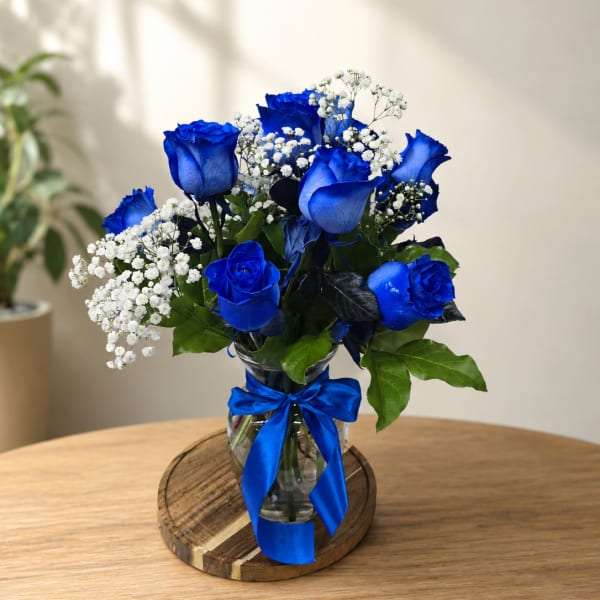 Blue roses and white baby's breath in a glass vase with a blue ribbon