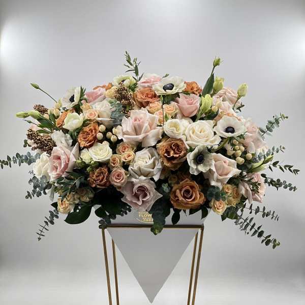 Large pastel floral arrangement in a white container on a gold stand