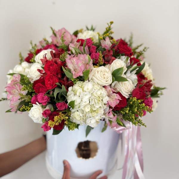 Mixed pink, red, and white flower arrangement in a white hat box with ribbon