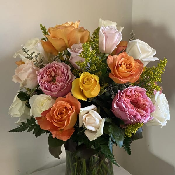Mixed roses in orange, pink, yellow, and white in a glass vase