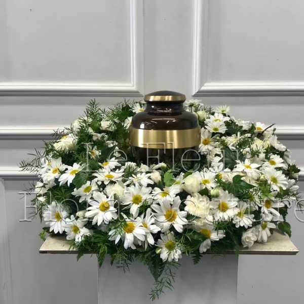 White daisy wreath around a dark urn with gold accents
