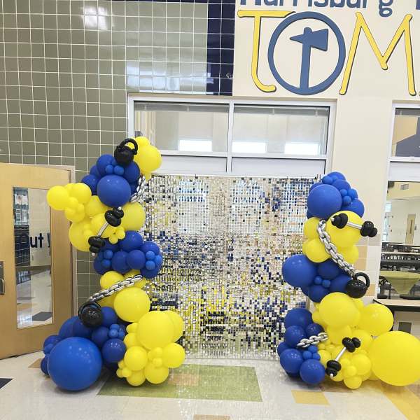 Blue and yellow balloon columns with black accents in a school hallway