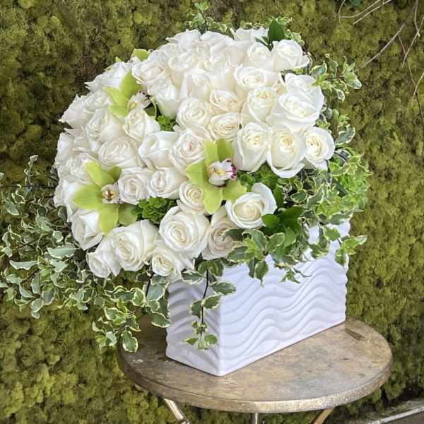 White rose arrangement in a white textured vase with trailing ivy
