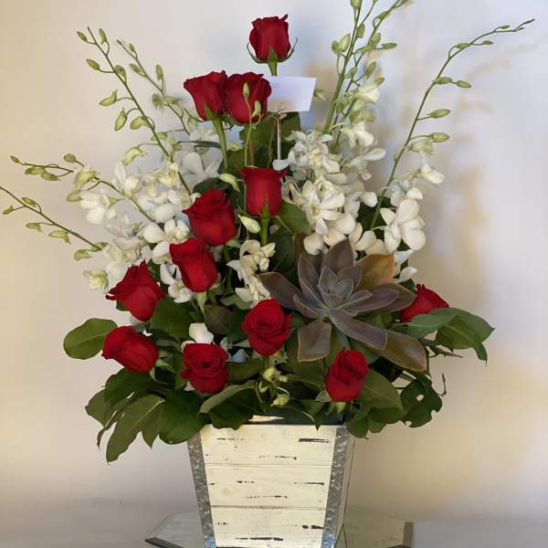 Red roses and white orchids in a tall silver planter with a succulent accent