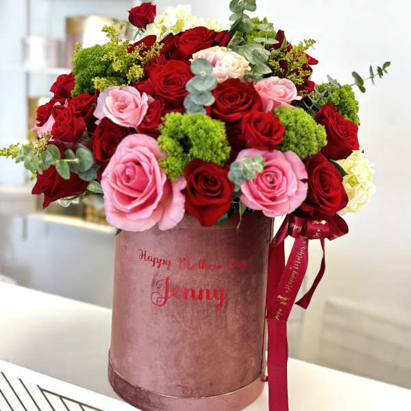 Red and pink roses arranged in a pink hatbox with ribbon