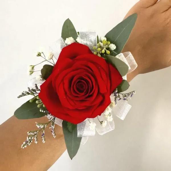 Red rose wrist corsage with white ribbon and greenery