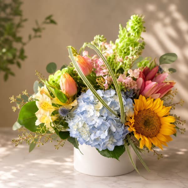 Mixed bouquet in a white vase with hydrangea, sunflowers, tulips, and pink blooms