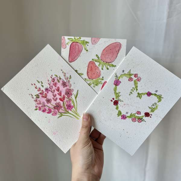 Hand holding three floral watercolor cards with pink designs