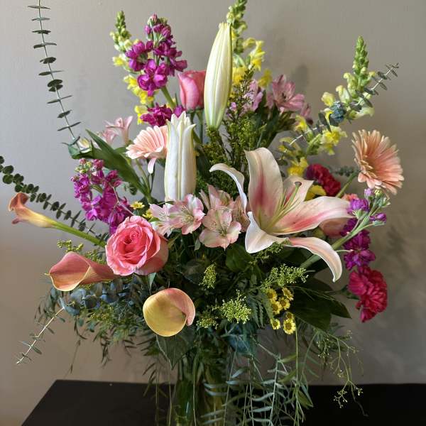 Mixed bouquet with pink roses, lilies, calla lilies, and purple blooms in a glass vase