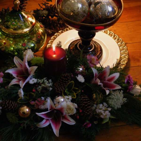 Holiday centerpiece with lilies, a red candle, and decorative ornaments
