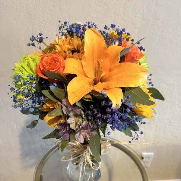 Bouquet of orange lilies, roses, and blue filler flowers in a glass vase