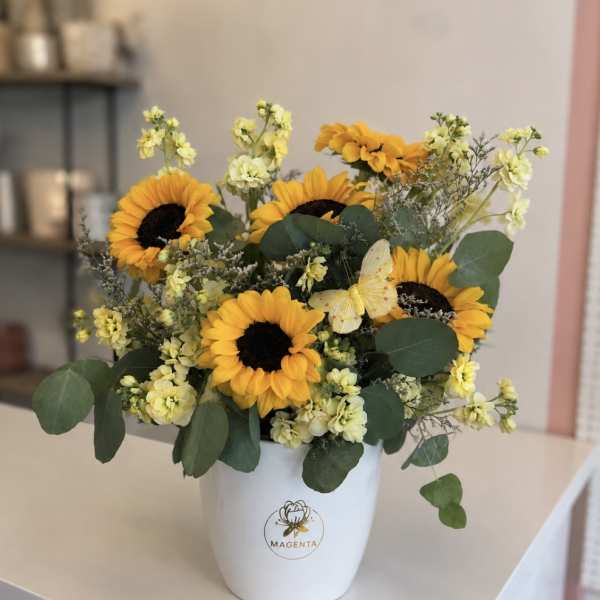 Sunflowers and pale yellow flowers arranged in a white vase