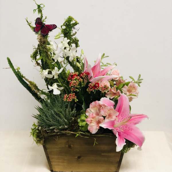 Pink lilies and white orchids in a wooden planter with moss and a butterfly accent