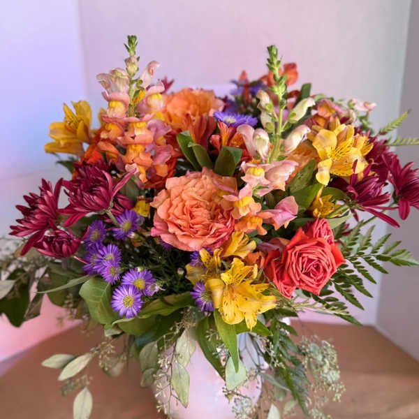 Mixed bouquet of pink, orange, yellow, and purple flowers in a white vase