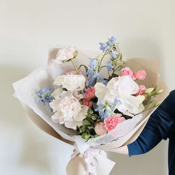 Hand-tied bouquet of pastel pink, white, and blue flowers wrapped in paper