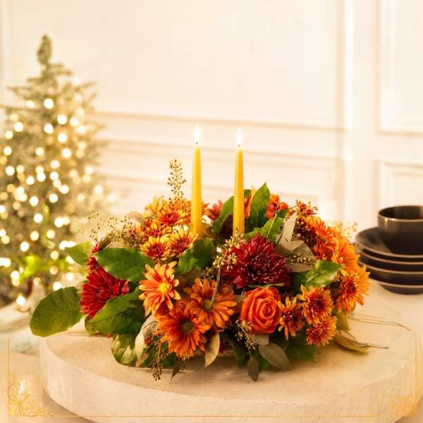 Autumn floral centerpiece with orange and red blooms and two taper candles
