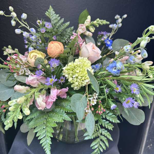 Pastel garden-style flower arrangement in a clear glass vase against a dark background