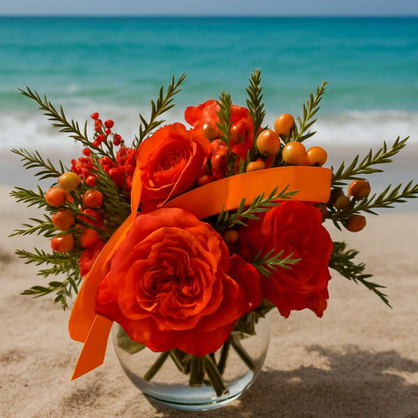 Orange rose bouquet in a clear glass vase with ribbon and berries