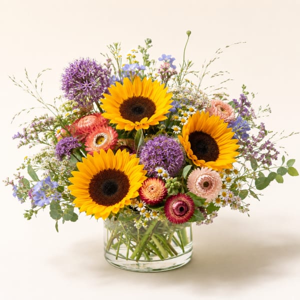 Mixed bouquet with sunflowers, purple blooms, and pink flowers in a glass vase