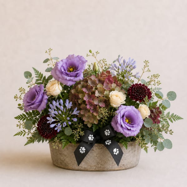 Mixed bouquet in a low stone container with purple, cream, and burgundy blooms