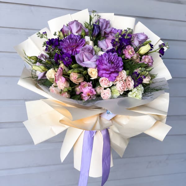 Bouquet of purple and pink flowers wrapped in cream paper with a lavender ribbon