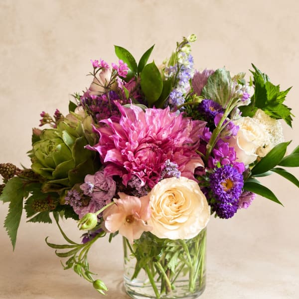 Mixed bouquet of pink, purple, and cream flowers in a clear glass vase