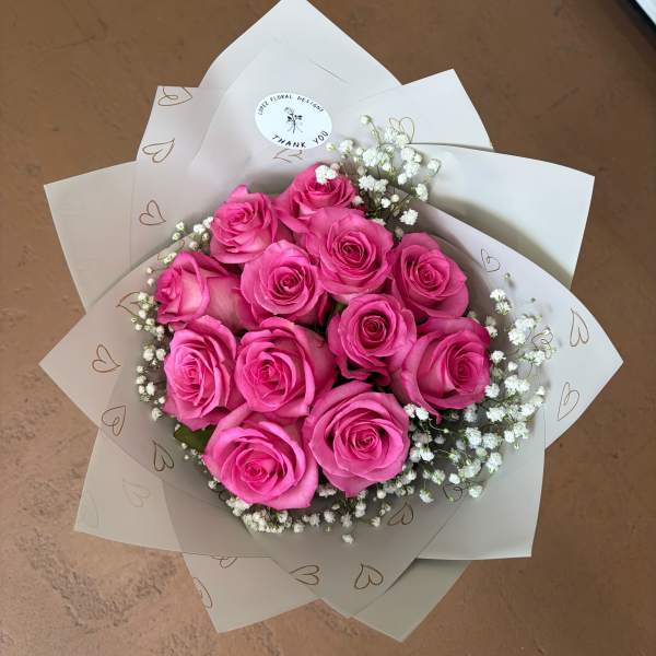 Bouquet of bright pink roses with white baby's breath in white wrap