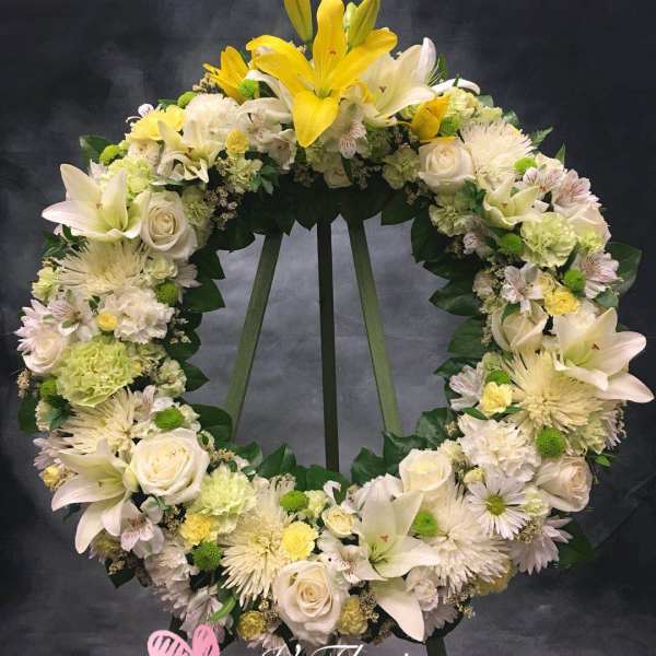 Standing wreath of white and yellow lilies, roses, and mums on a green easel