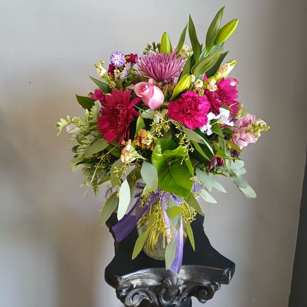 Mixed pink and purple bouquet in a glass vase with a purple ribbon