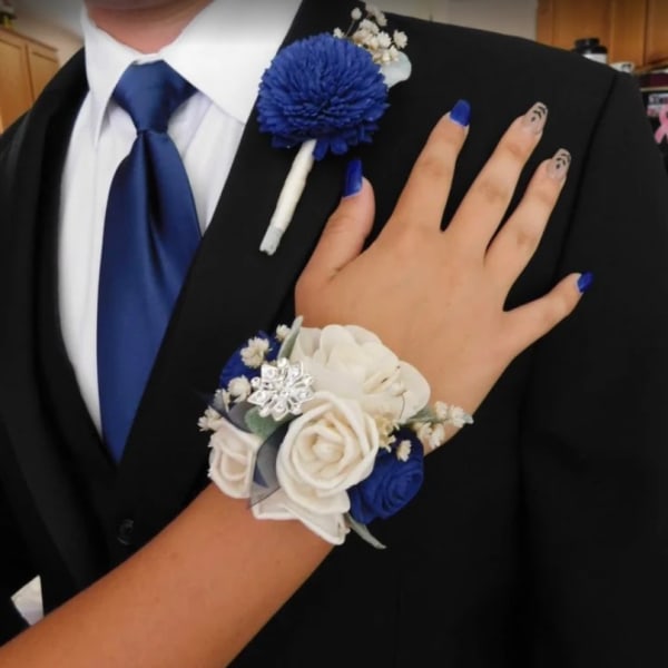 Blue and white wrist corsage with matching boutonniere on a black suit with blue tie.