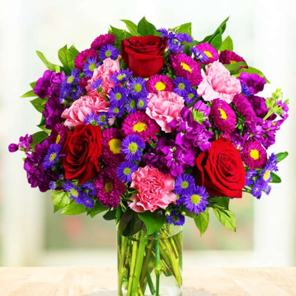 Bouquet of red roses, pink carnations, and purple daisies in a glass vase