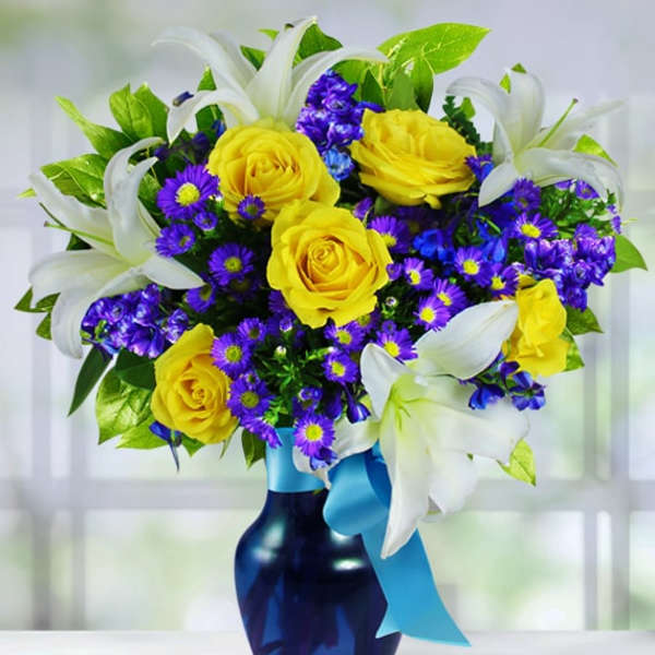 Bouquet of yellow roses, purple flowers, and white lilies in a blue vase