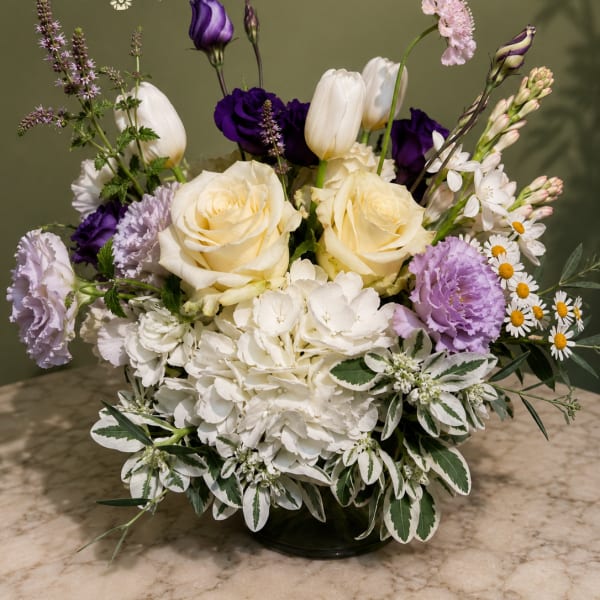 Bouquet of cream roses, white hydrangea, and purple blooms in a low vase