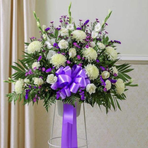 Large white and purple floral standing arrangement with a purple ribbon