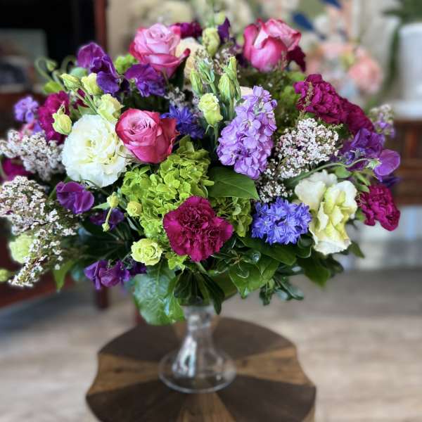Mixed bouquet of pink, purple, white, and green flowers in a glass vase