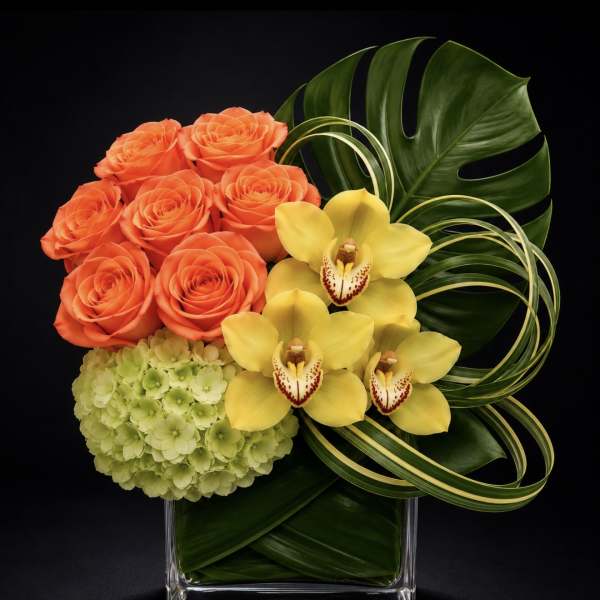 Orange roses, yellow orchids, and green hydrangea in a clear square vase