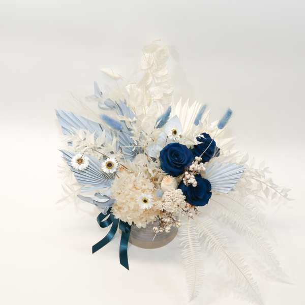 Blue and white floral arrangement in a round container with ribbon
