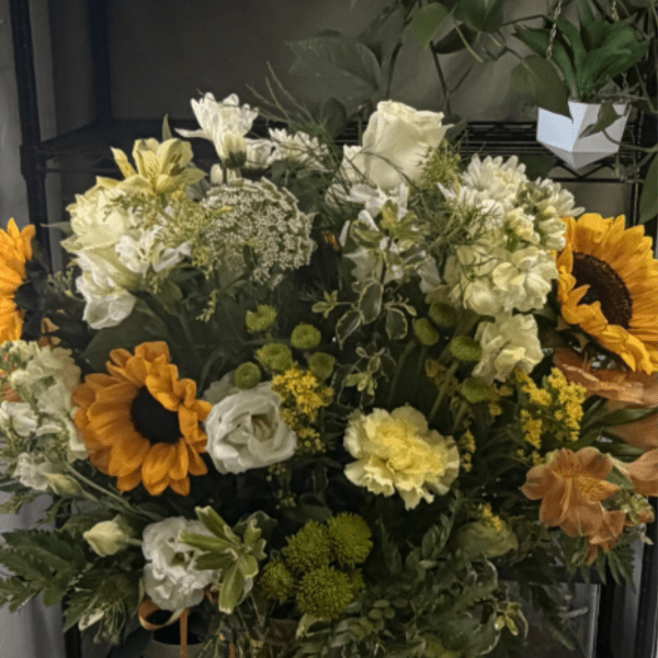 Large mixed bouquet in a clear glass vase with sunflowers and white blooms