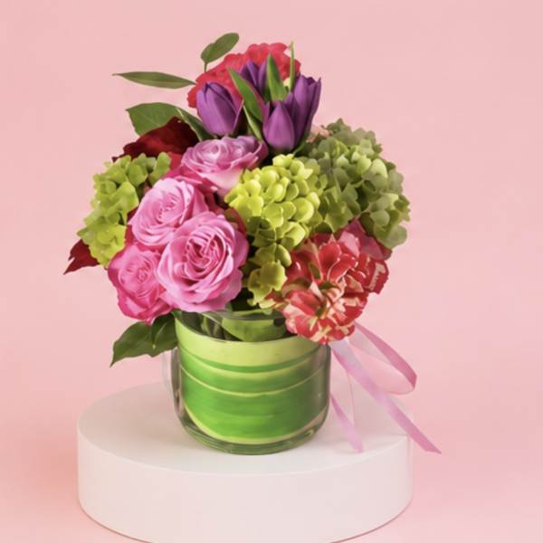 Pink and purple bouquet in a glass vase with a pink ribbon