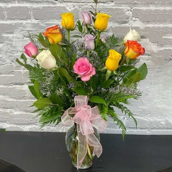 Bouquet of multicolored roses in a glass vase with a pink ribbon