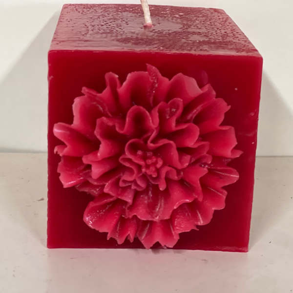 Red square candle with a large flower decoration on the front