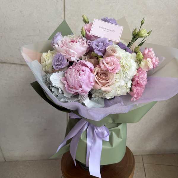 Pastel bouquet of pink, lavender, and white flowers wrapped in green paper