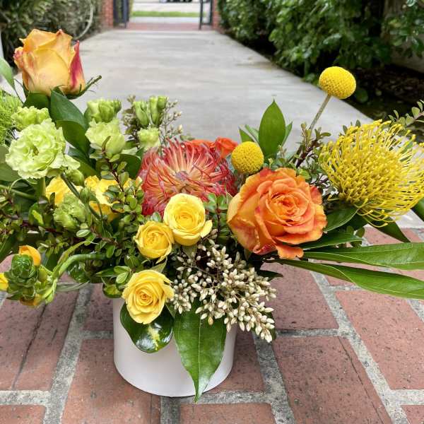 Colorful mixed flower arrangement in a white vase with roses and tropical blooms