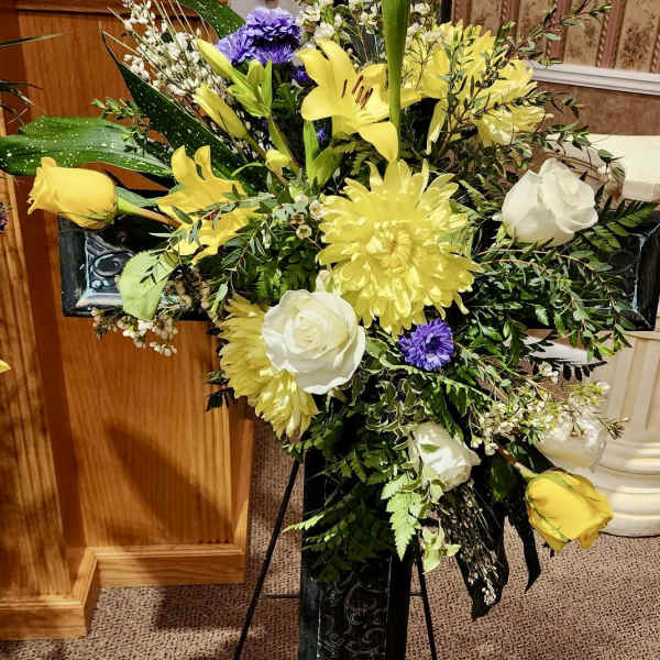 Standing floral spray with yellow and white flowers on a black easel