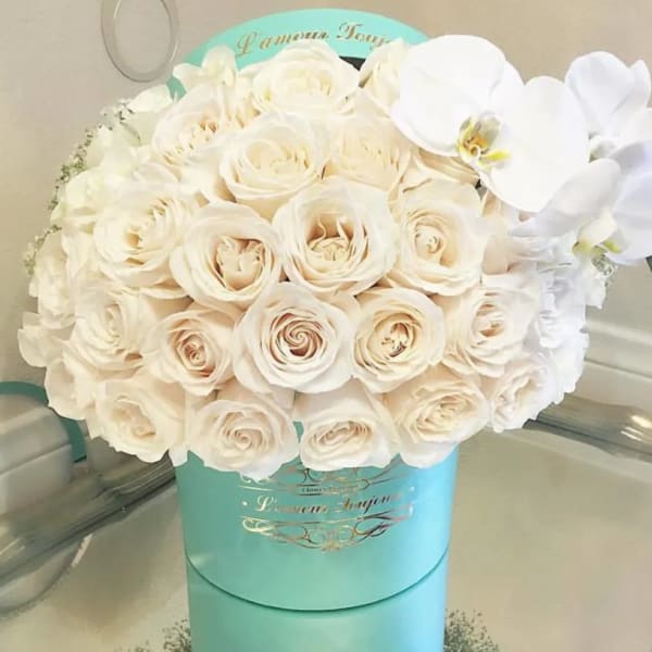 White roses and orchids arranged in a turquoise hat box