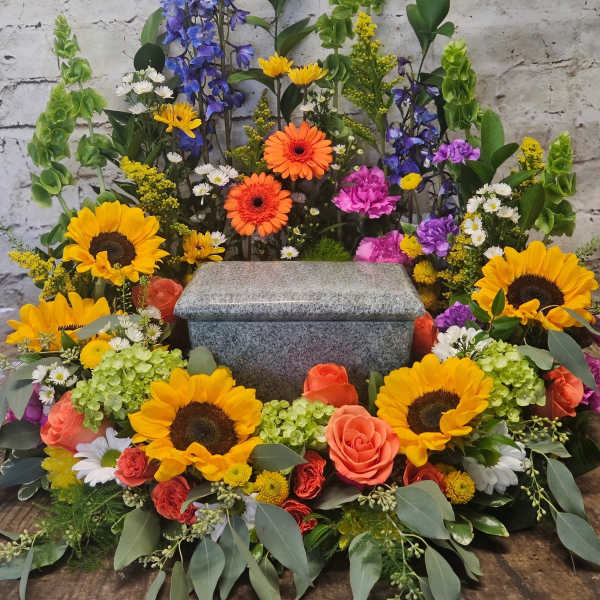 Colorful funeral spray around a gray granite urn with sunflowers and roses