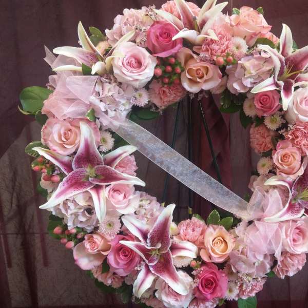 Heart-shaped floral wreath with pink roses and lilies on a stand