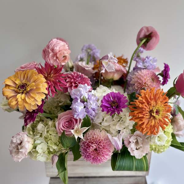 Mixed bouquet of pink, orange, and lavender flowers in a wooden box