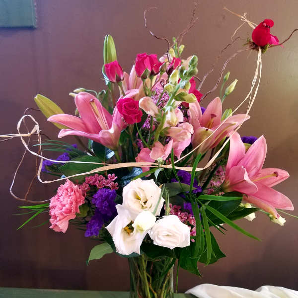 Pink lilies, roses, and white blooms arranged in a glass vase